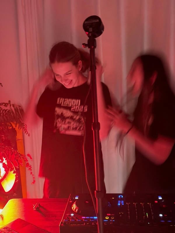 Me grinning in front of a DJ controller while taking off headphones, with a very blurry jumping girl next to me.